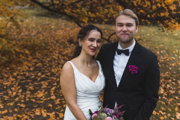 Lovely happy ethnic couple - Turkish woman and Scandinavian man - posing for her wedding day photoshoot in beautiful autumn park covered with orange leaves. High quality photo