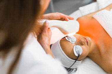 Profesyonel termokaldırıcı yüz. Kırışıklıkların azaltılması. Deri sıkışıyor. Tanımlanamayan bulanık güzellik uzmanları. SPA yüz bakımı sırasında koruyucu gözlüklü genç bir kadın. Yüksek kalite fotoğraf
