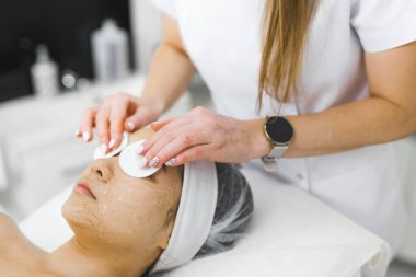 Tanınmayan güzellik uzmanı, genç Asyalı müşterisinin göz bölgesindeki temizleme maskesini pamuk kozmetik pedlerle çıkarıyor. Cilt bakımı. - Evet. Yüksek kalite fotoğraf