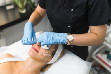 Yüz bakımı konsepti. Tanımlanamayan beyaz kadın güzellik uzmanı koruyucu eldivenlerle kadın müşterisine cilt bakımı yapıyor. Yüksek kalite fotoğraf