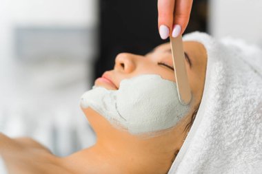 Masada uzanmış genç bir Asyalı kadının yakın plan çekimleri. Rahatlamış ve bir profesyonel ona yüz maskesi yapıyor. Kozmetoloji merkezi. Yüksek kalite fotoğraf