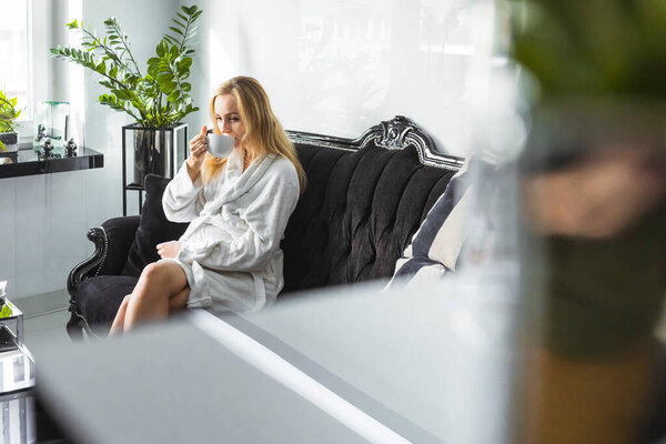 beautiful blond pregnant woman in a white robe drinking tea in the wellness spa center, medium full shot bodycare concept. High quality photo