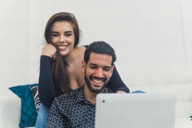 Güzel, mutlu, gülümseyen genç bir çift birlikte oturuyor, bilgisayarla görüntülü sohbet yoluyla birileriyle sarılıyor, sohbet ediyorlar. Yüksek kalite fotoğraf