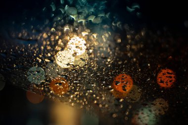 Şehir trafik ışıklarının soyut arkaplanı bulanık ve nemli, yağmur damlalarıyla dolu pencerelerden görülebiliyor. Şehirde yağmurlu bir hava var. Işıklarla oynuyorum. Yüksek kalite fotoğraf