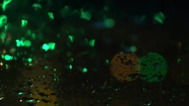 Şehirde gece yağmurunu görmenin alışılmadık bir yolu. Geceleri şeffaf pencereye yağmur damlaları düşer yeşil, sarı ve kırmızı renkte bulanık şehir ışıklarıyla. Yüksek kalite 4k görüntü