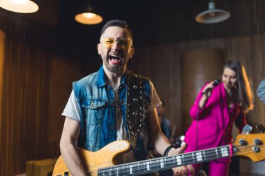 Kotsuz yelek giyen, elektro gitar tutan ve çığlık atan beyaz bir adam. Kapalı çekim. Grup kayıt stüdyosunda. Yüksek kalite fotoğraf