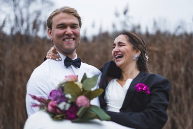 Genç damat, kollarında beyaz bir elbiseyle neşeli gelinini tutuyor. Açık havada düğün fotoshop 'u. Yüksek kalite fotoğraf