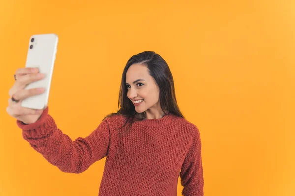 stock image medium shot of an attractive girl holding a phone and taking a selfie, studio shot isolated on orange background medium shot. High quality photo