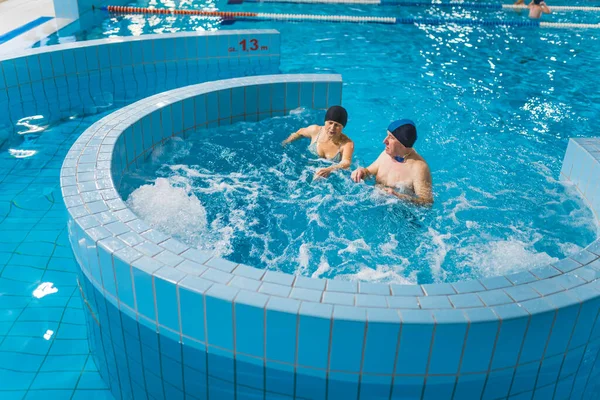 Variety of pool park swimming pools. Couple of caucasian pensioners or grandparents actively spending their free time by swimming in lazy river and jacuzzi. High quality photo