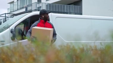 Genç siyah teslimatçı müşterilerin evine beyaz minibüsten boşaltılmış karton kutuyla gidiyor. - Evet. Yüksek kalite 4k görüntü