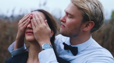 Sevgili Orta Doğulu karısının gözlerini kapatan 20 'li yaşlarının sonlarında sarışın, yakışıklı İskandinav damat. Orta boy dış mekan portresi. Aşk ve romantizm. Yüksek kalite 4k görüntü