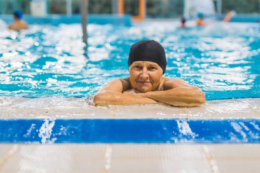 Sağlık ve aktif vücut bakımı konsepti. Yüzme havuzunda dinlenen, siyah yüzme şapkalı, beyaz, arkadaş canlısı bir kadının portresi. Yüksek kalite fotoğraf