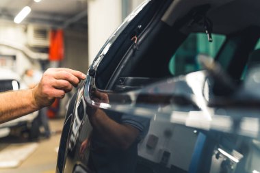 Tamirhanedeki araç camları kaldırma işlemi. Siyah bir arabadan yapışkan kalıntılarını çıkaran tanınmamış beyaz bir tamircinin eli. Yüksek kalite fotoğraf