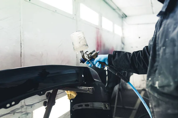 White spray booth interior. Process of automobile painting. Car fender varnishing. Unrecognizable person in protective coveralls using paint spray gun. High quality photo