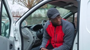 Kırmızı kazaklı, siyah şapkalı genç bir teslimatçı beyaz minibüsün kapısında kameraya doğru gülümsüyor. Yüksek kalite 4k görüntü