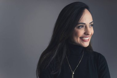 Geniş dişli bir gülüşü olan zarif genç bir kadının orta boy yakın çekimi, yanında gri arka plan stüdyo fotoğrafı. Yüksek kalite fotoğraf