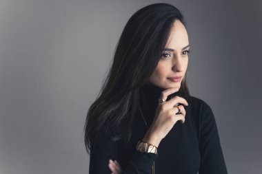 Koyu saçlı bir kızın, üzerinde kafa yorarken ve ona bakarken orta boy yakın plan çekimi. Gri arka plan. Yüksek kalite fotoğraf