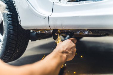 Mekanik çalışmada ekipmana ihtiyaç var. Araba tamiri. Metal şaseyi kesmek için öğütücü kullanılarak korunmasız kafkas kolunun düşük açılı görüntüsü. Yüksek kalite fotoğraf