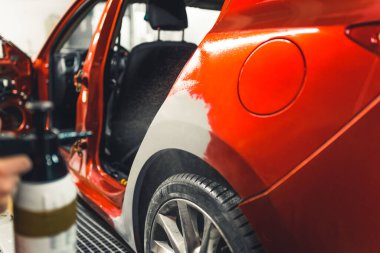 Otomotiv dolgusu uygulamak için kullanılan bulanık sprey ayakkabı. Bir kısmı araba boyamaya hazırlanan kırmızı arabanın kapalı çekimleri. Yüksek kalite fotoğraf
