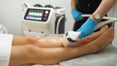 SPA ve Güzellik Salonu tedavisi - bacaklardan lazer tüyü alınması. Kafkasyalı müşterisine lazer kullanarak koruyucu mavi eldivenli, tanınmaz hale gelen beyaz güzellik uzmanı. Saç temizleme kozmetoloji prosedürü
