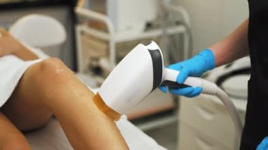 SPA ve Güzellik Salonu tedavisi - bacaklardan lazer tüyü alınması. Kafkasyalı müşterisine lazer kullanarak koruyucu mavi eldivenli, tanınmaz hale gelen beyaz güzellik uzmanı. Saç temizleme kozmetoloji prosedürü