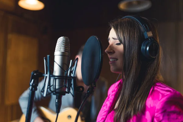 Portrait of vocalist recording a song with headphones on. Closeup indoor portrait of caucasian female singer singing to professional microphone with closed eyes. High quality photo