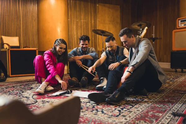 Band creating a song. Four member band with two guitarists, a drummer, and female vocalist sitting on carpet inside the recording studio. High quality photo
