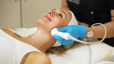 Siyah üniformalı, tanınmayan bir güzellik uzmanı tarafından yapılan mikro dermabrüksiyon işlemi sırasında beyaz kolsuz tişörtlü çekici sarışın beyaz kadının kapalı çekim özelliği. Yüksek kalite 4k görüntü