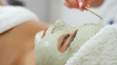 SPA günü ve rahatlama konsepti. Derin cilt temizliği. Asyalı bayan müşterisinin yüzüne kilden maske takan tanınmamış Kafkas güzellik uzmanı. Yüksek kalite 4k görüntü