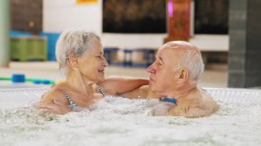 Hoş yaşlı beyaz çift boş zamanlarını sıcak bir banyo havuz kompleksinde dinlenerek geçiriyorlar. Su yüzeyi perspektifi Yüksek kalite 4k görüntü