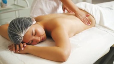 Rahatlatıcı ve rahatlatıcı sırt masajı. 20 'li yaşlarda, koruyucu saç şapkalı Asyalı bir kadın profesyonel sırt masajı sırasında en sevdiği SPA' da yüzüstü yatıyor. Yüksek kalite 4k görüntü