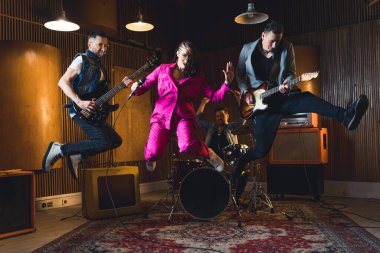 Full-length indoor shot of music band jumping. Lead singer and two guitarist jump in the air. Recording studio or garage studio interior. High quality photo clipart
