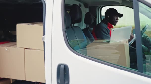Nuori Aikuinen Musta Lähetti Istuu Valkoisen Pakettiauton Kuljettajan Istuimella Katsomassa — kuvapankkivideo