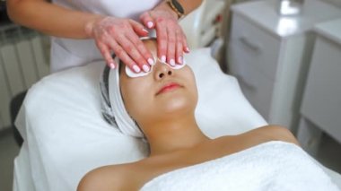 SPA tesisinde yüz temizleme. Genç, güzel bir Asyalı kadın göz rahatlatıcı bir işlem sırasında saçında koruyucu bantla SPA yatağında uzanıyor. Yüksek kalite 4k görüntü
