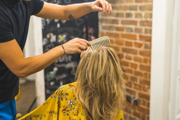 Professional male hairdresser spraying and styling with comb his female clients blonde hair in the professional hair salon. High quality photo