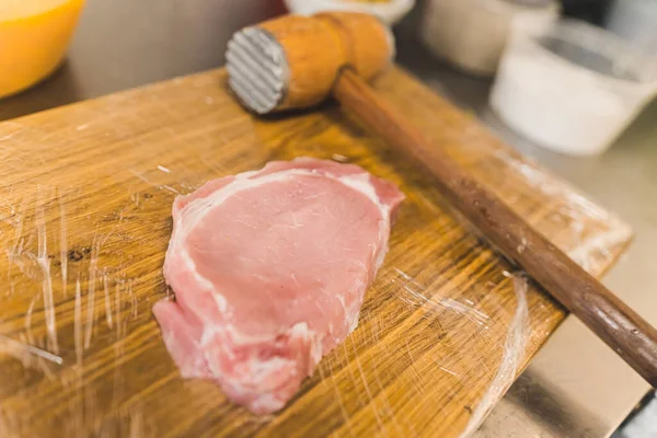 Raw pork chop on wooden board. Piece of uncooked pork chop cutlet next to wooden and metal beater. High angle indoor shot. High quality photo