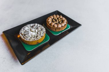 Siyah tabakta beyaz masada servis edilen iki minyatür tatlı turtası. Çikolatalı ganache meyveleri pudra şekeri. Güzel pişmiş yiyecekler. Yatay çekim. Yüksek kalite fotoğraf