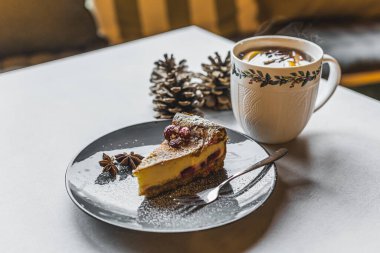 Tabakta pudra şekeri ve anason yıldızlarıyla servis edilen vişneli cheesecake. Bir fincan sıcak çay. Çam kozalağı süslemesi. Noel pastası. Bayramlık tatlı. Kapalı alanda yatay çekim. Yüksek kalite fotoğraf