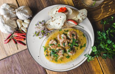 Baharatlı soslu karidesler ekmekle servis edilir. Üst Manzara. Tahta masadaki beyaz tabak. Restoran yemeği konsepti. Yüksek kalite fotoğraf