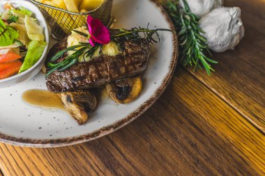 Mantarlı biftek ve yanında salata ve patates kızartması. Ahşap masada etli tabak. Yüksek kalite fotoğraf