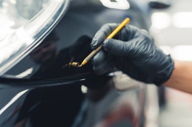 Eldivenli eldiven kapağı bir garajda arabanın ön kısmındaki küçük göçüğü temizliyor. Araba tamiri. Kapalı alanda yatay çekim. Yüksek kalite fotoğraf