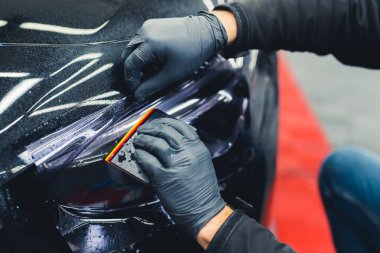 Bir garajdaki arabanın farına PPF boya koruması uygulayan siyah eldiven takan birini yakın plan çek. Araba tamiri. Kapalı alanda yatay çekim. Yüksek kalite fotoğraf