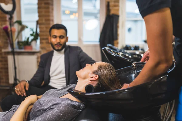 barber washing womans hair at the salon and her husband waiting hr her on the couch. High quality photo