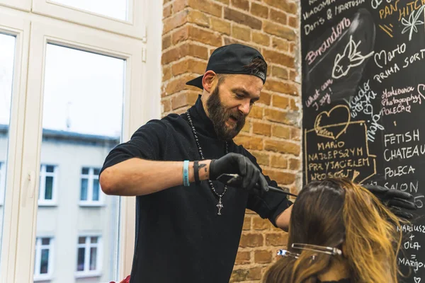 Absorbed hairdresser in the black hat with beard styling his clients long hair in the professional hair salon. . High quality photo