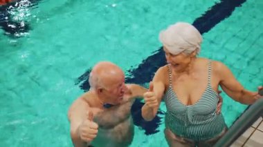 Yaşlı emekli çift yüzme havuzunda kameraya baş parmak gösteriyor. Yüksek kalite 4k görüntü