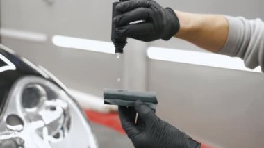 İşten önce siyah bir süngerin boyasına seramik kaplama uyguluyorum. Arka planda siyah araba var. Arka plan bulanık. Yüksek kalite 4k görüntü