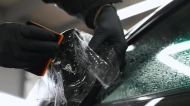 Siyah eldiven giyen birinin aynanın dışındaki siyah arabalara boya koruyucu film takması. Yüksek kalite 4k görüntü