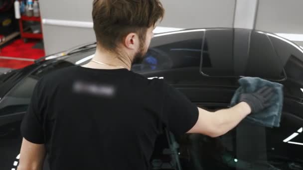 身穿黑色T恤 留着胡子的男子在专业汽车沙龙的一辆黑色轿车上涂上陶瓷涂层 Madium Shot 是的高质量的4K镜头 — 图库视频影像