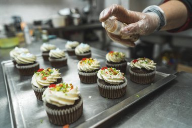 Beyaz kremayla süslenmiş kekler ve mutfakta bir kişi tarafından hazırlanan renkli parıltılar. Şeffaf bir eldiven verin. Arka plan bulanık. Yüksek kalite fotoğraf