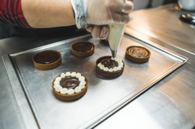 Pasta tepsisine yerleştirilmiş turtalar pasta poşeti kullanan biri tarafından beyaz kremayla süsleniyor. Şeffaf eldiven giyen bir fırıncı. Arka plan bulanık. Yüksek kalite fotoğraf